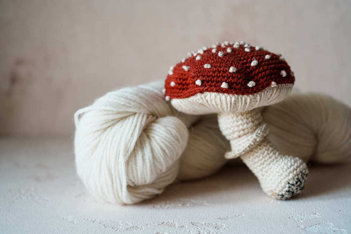 A white ball of yarn with a crocheted red mushroom on top