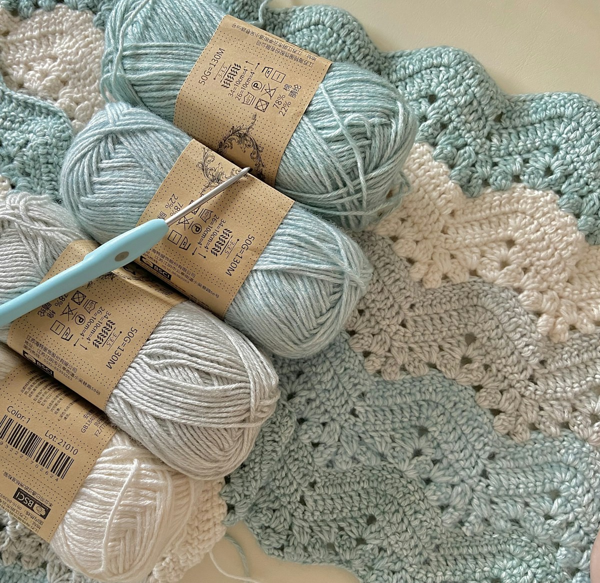 Three balls of yarn and a crochet hook resting on a blanket